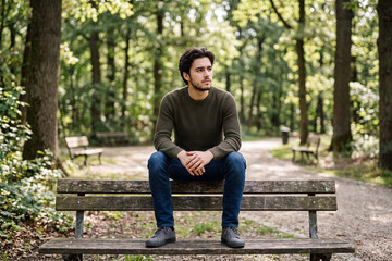 Fototapeta premium Young Man Sits Alone on Park Bench Lost in Deep Thought and Quiet Internal Struggle