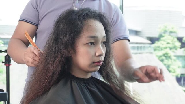 Hair stylist sectioning and combing hair with tail comb before hair coloring treatment in salon for Southeast Asian woman in her early 20s
