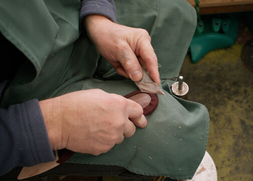 Handmade craft. Shoe repairing. Unrecognizable professional cobbler man hands working with sole using knife in artisan factory.