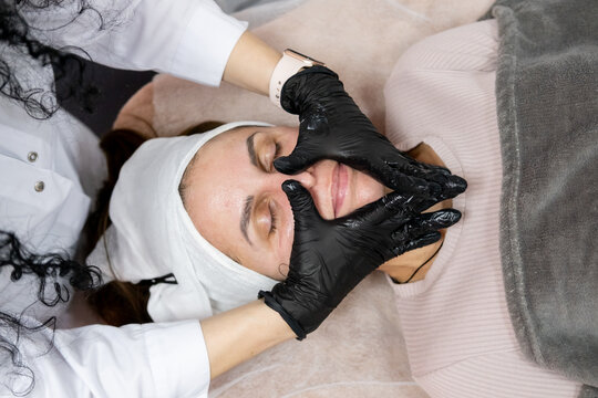 Face massage. Cosmetologist occupation. Female professional masseur beauty specialist in gloves using product for treatment in salon.
