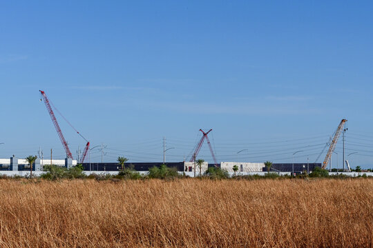 Large data center campus under construction with cranes beyond undeveloped land and dry vegetation, illustrating digital infrastructure, land development, and suburban expansion
