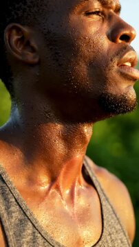 Close-up of a determined Black man sweating profusely after an intense outdoor workout, his skin glistening under the sun, embodying peak physical effort and dedication