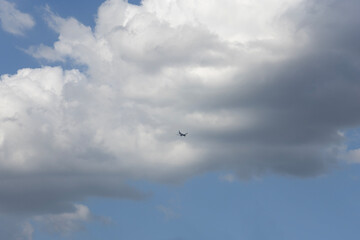 Fototapeta premium Airplane flying high in the blue sky surrounded by large white clouds