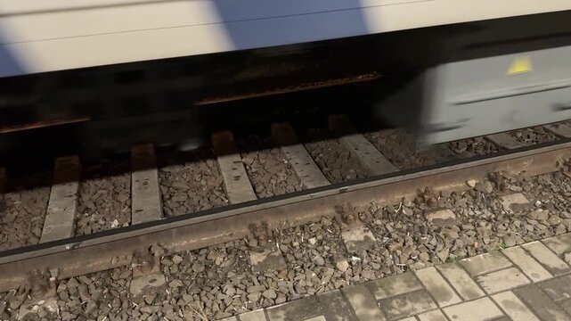 High speed train wheels passing by on railway tracks. Static overhead shot capturing mechanical motion of metal carriages moving past the platform.