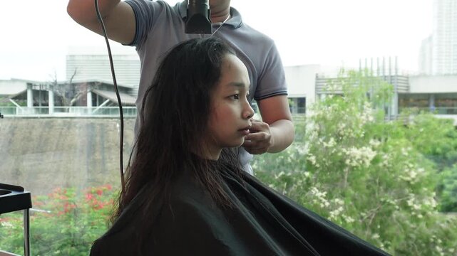 Hair stylist blow drying long hair before hair coloring treatment in salon for Southeast Asian woman in her early 20s