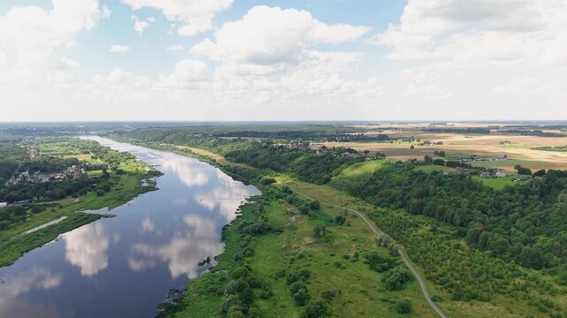 Stunning aerial footage captures a tranquil river meandering through lush green countryside, bordered by fields and forest. Bright daylight, blue sky, and fluffy clouds add a peaceful, natural mood.