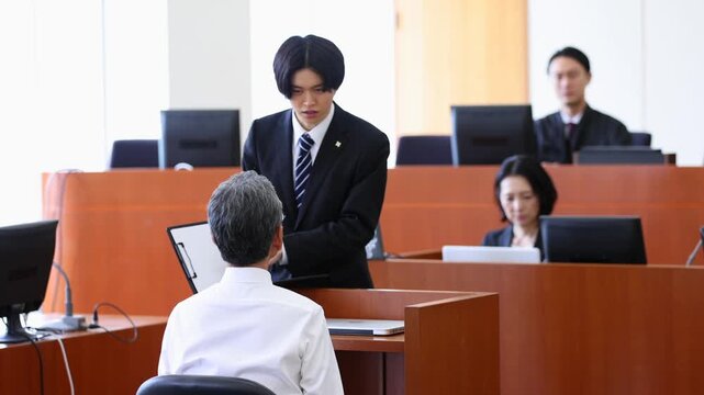 法廷で証拠資料を示しながら証人に説明する若い検察官