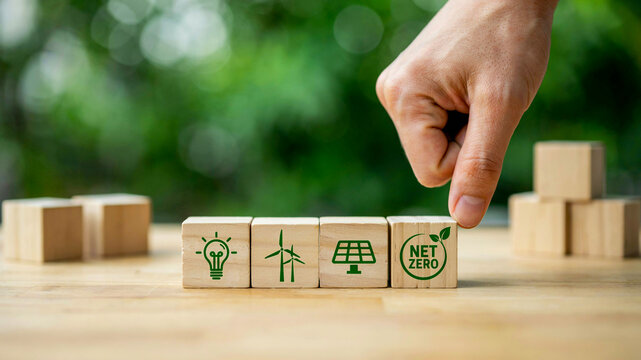 Hand arranging wooden blocks with renewable energy symbols and 'NET ZERO' concept, symbolizing commitment to sustainable future, environmental protection, and carbon neutrality for a greener planet