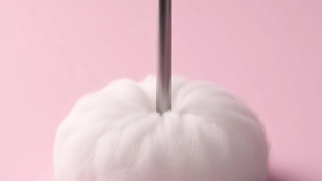 A metal tool piercing a soft white steamed bun on a pink background.