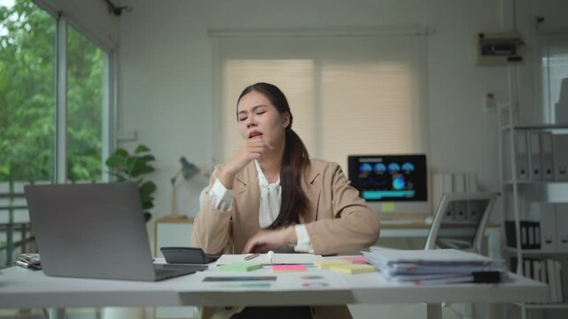 Overworked asian office worker feeling tired and frustrated while sorting through a large stack of documents and financial reports, eventually experiencing a headache from the stress