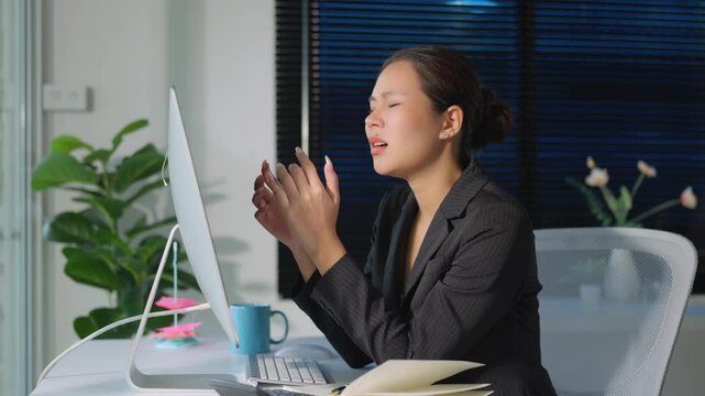Frustrated Asian businesswoman reacting to bad news on her computer, showing disappointment and stress while working overtime in a dark office, eventually holding her head in despair