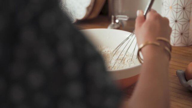 Person whisks dry ingredients inside a ceramic bowl while preparing a delicious homemade cake recipe in a modern kitchen environment, focusing on the rhythmic motion of culinary baking activities.