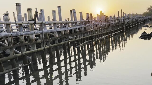 Traditional bamboo bridge structure on water reflecting a warm golden sunrise