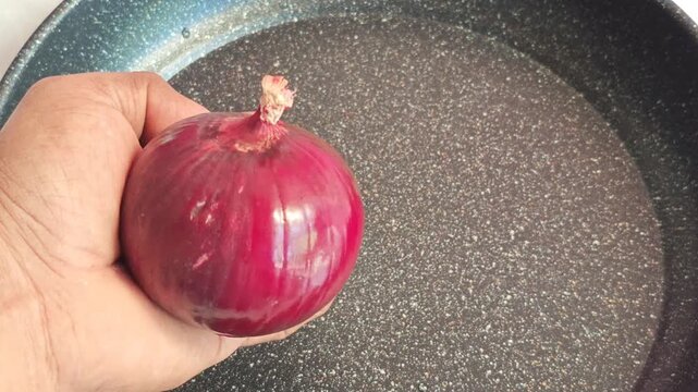 Hand Holding Red Onion with Frying Pan in Background