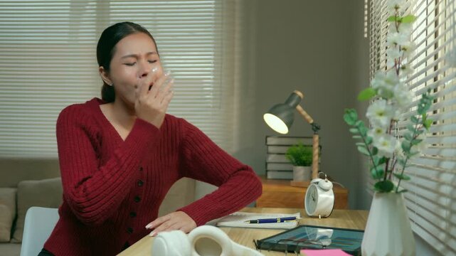 Exhausted young woman yawning and feeling sleepy while studying or working late at night, eventually falling asleep on her desk due to burnout and fatigue after a long day of work from home