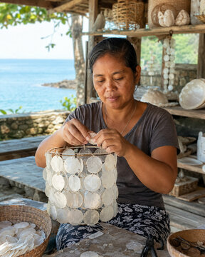 Asian female artisan assembling a beautiful handmade capiz shell lamp in a coastal workshop