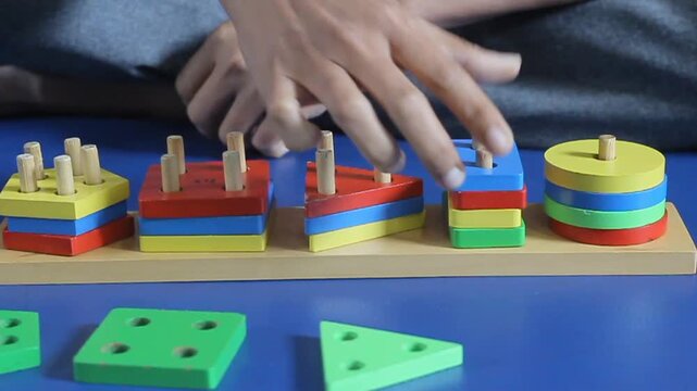 A person stacking colorful wooden geometric shapes onto pegs