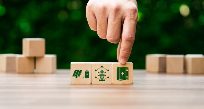 Smart grid and battery storage concept with hand placing power cabinet icon cube on wooden pyramid blocks showing renewable energy infrastructure and sustainable electricity management