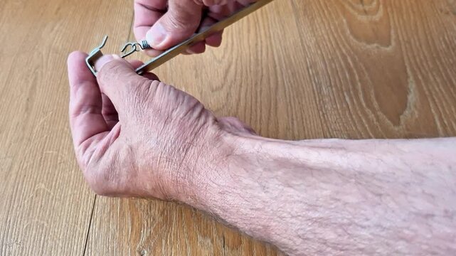 Disconnecting a tension spring from a metal hook by hand with controlled force, demonstrating a simple mechanical fastening release. Ideal for repair, maintenance, DIY, engineering