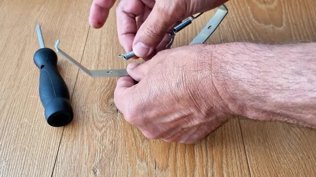 A hand carefully attaches an extension spring to a metal hook, demonstrating a simple mechanical fastening process with steady motion, ideal for repair, assembly, and DIY concepts