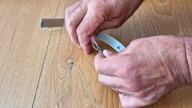 Hand safely removes extension spring from metal hook, highlighting careful handling, mechanical maintenance, and proper technique for household repair and equipment upkeep