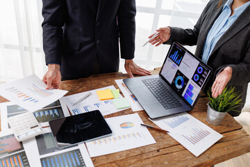 Naklejka na ściany i meble Business professionals analyzing financial data dashboard on a laptop, collaborating during a corporate meeting, discussing annual reports and market strategy on a wooden desk