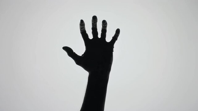 Zombie hand silhouette reaching out. Spooky monster claw gesture in slow motion.
