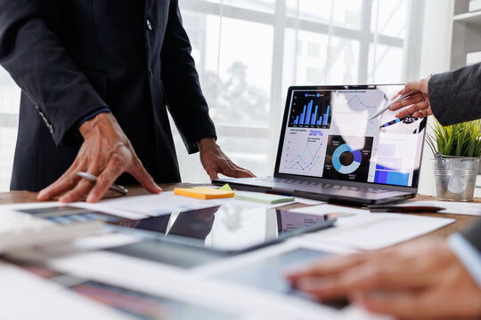 Business professionals collaborating at a meeting. Reviewing complex financial data and analytics displayed on a laptop screen. Discussing charts. Graphs