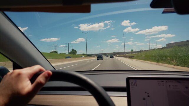 POV wide inside view of electric vehicle cruising on a multi-lane highway during a sunny summer day. Interior dashboard with steering wheel