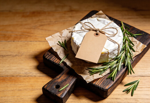 Camembert cheese, brie wheel, artisanal dairy product, rustic wooden board, blank price tag, gourmet food photography, fresh rosemary, organic brie wheel, craft paper label, wooden table, dairy food.