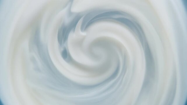 White milk swirls through clear water, forming soft cloudlike tendrils and gentle spiral motion under even overhead lighting with clean cinematic macro texture.