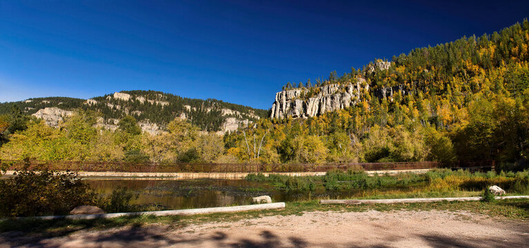 Pano of limestone rocks on a hill with colorful trees above a bridge on a sunny autumn day Spearfish Canyon, South Dakota.