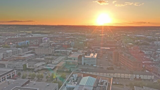Doncaster town centre extends across South Yorkshire, England, United Kingdom, with dense commercial streets, civic buildings and urban districts at golden sunset, drone forward flyover.