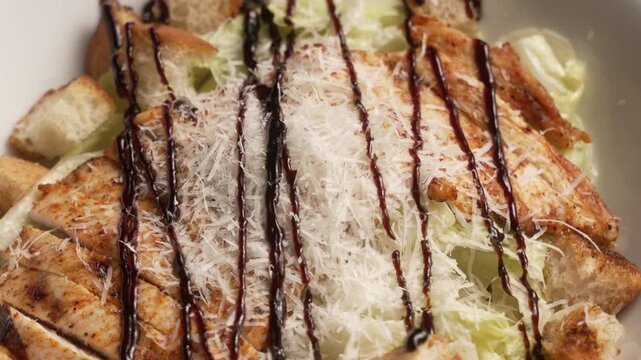 Delicious chicken caesar salad spinning in a white bowl with parmesan cheese and balsamic dressing