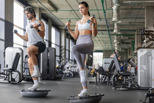 Athletic couple doing single-leg balance exercise on BOSU ball at gym