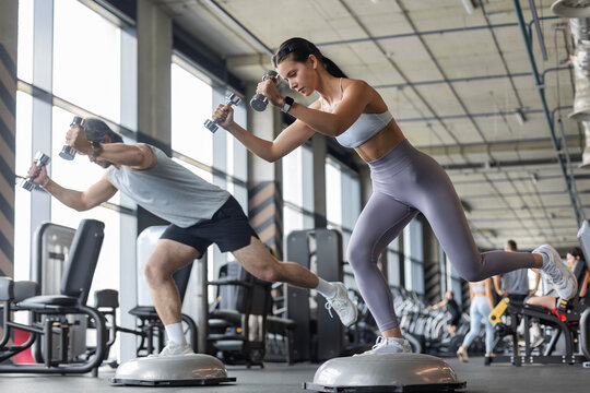 Athletic couple doing single-leg balance exercise on BOSU ball at gym