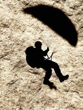 Silhouette of a Military Paratrooper Descending Against a Rugged Textured Cliffside Background for Tactical Aviation Concepts