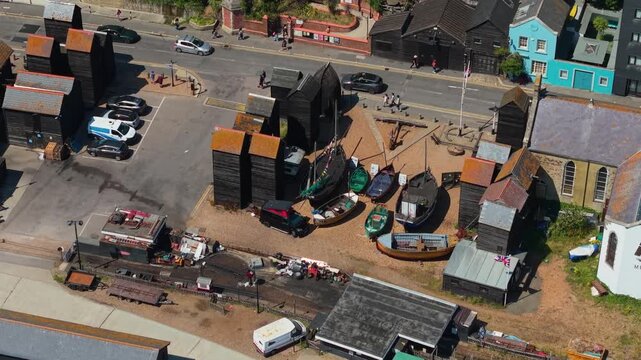 Iconic tall black wooden net shops, traditional fishing boats, and historic maritime heritage area at the Stade beach in Old Town Hastings, East Sussex, UK, seen by aerial drone orbit.