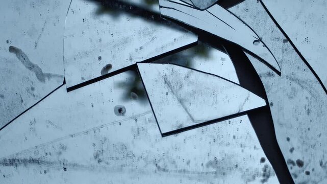 Broken dirty glass mirror shards with sharp edges reflecting light on a textured surface