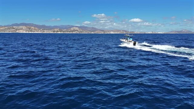 Drone tracks a fishing boat racing over the water back toward the coastline off the East Cape of Baja California Sur, with the boat to the right and the shore to the left.