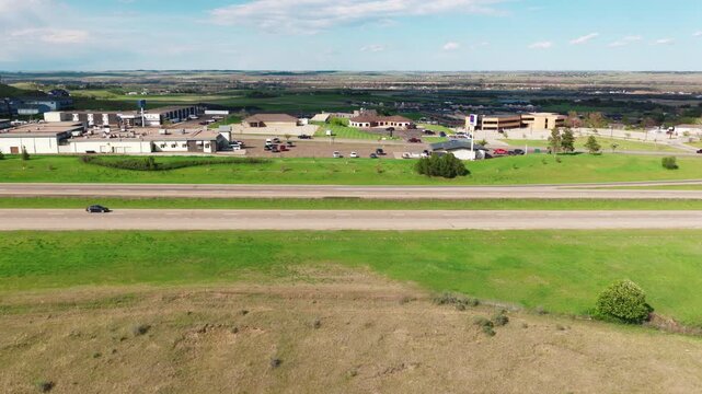 Mandan North Dakota commercial outskirts bordering the interstate. Rural town businesses and parking lots surrounded by green grass and rolling hills.