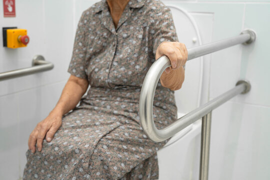 Asian elderly woman use toilet security support rail in bathroom.
