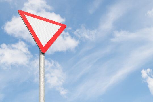 A yield traffic sign stands tall against a backdrop of a bright blue sky with white clouds