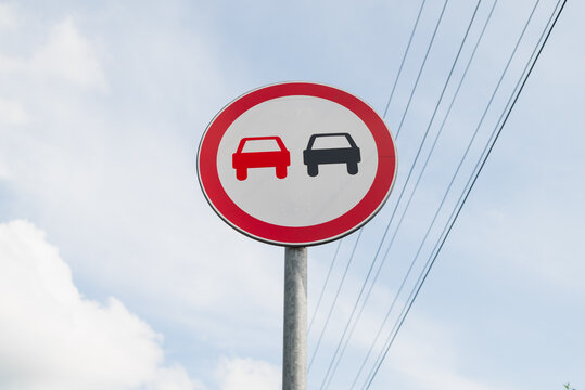 A traffic sign displays symbols of two cars, one in red and one in black, indicating no overtaking allowed.