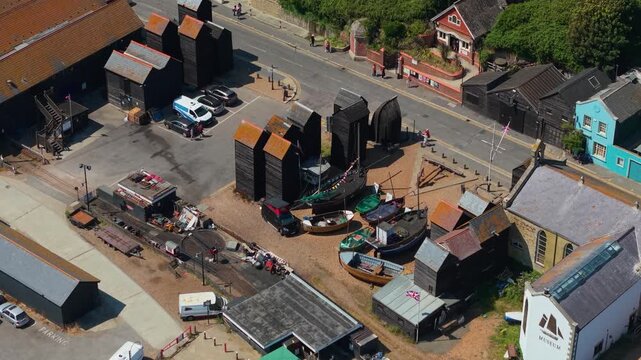 Iconic tall black net shops, traditional fishing boats, and coastal heritage architecture at the Stade in the historic Old Town of Hastings, UK, seen by slow forward drone.