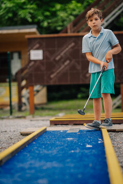 Boy playing minigolf on blue course during summer leisure
