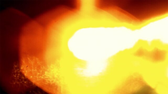 Molten glowing metal being poured in industrial foundry setting.