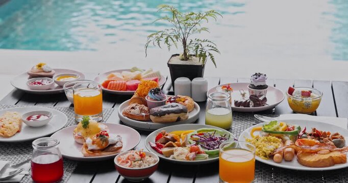 Breakfast dishes including eggs benedict, pastries, and fruits spread on table by swimming pool, luxury resort dining, morning brunch hospitality background