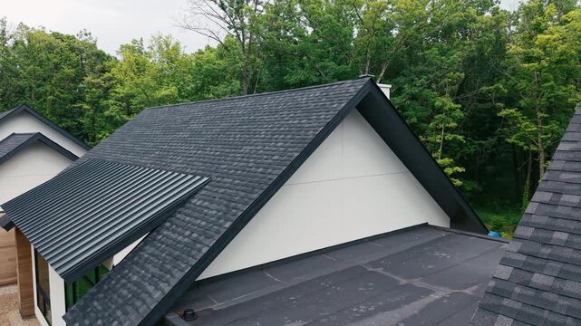 Modern residential roof of house with a newly installed black asphalt shingle roof surrounded by mature forest. 