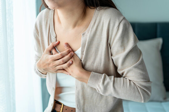 Young woman pressing her hands against her chest in pain, suffering from sudden chest pain or heart attack.